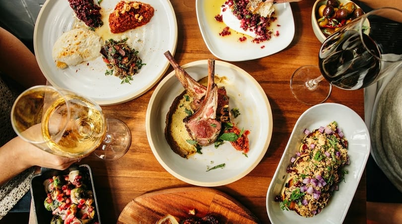 Overhead view of a wooden table laden with various Mediterranean dishes and wine glasses.
