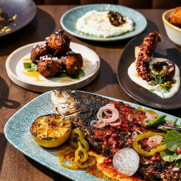 A table laden with various Mediterranean dishes, including whole grilled fish, octopus, olives, and salads.