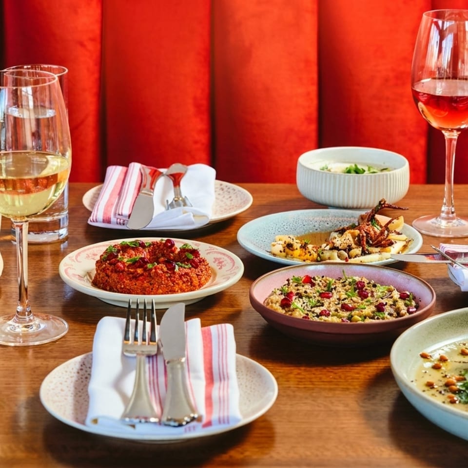 A wooden table laden with various Middle Eastern dishes, wine, and water against a red background.