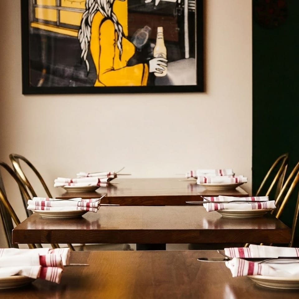 Set tables with white and red striped napkins, gold chairs, and a painting of a woman.