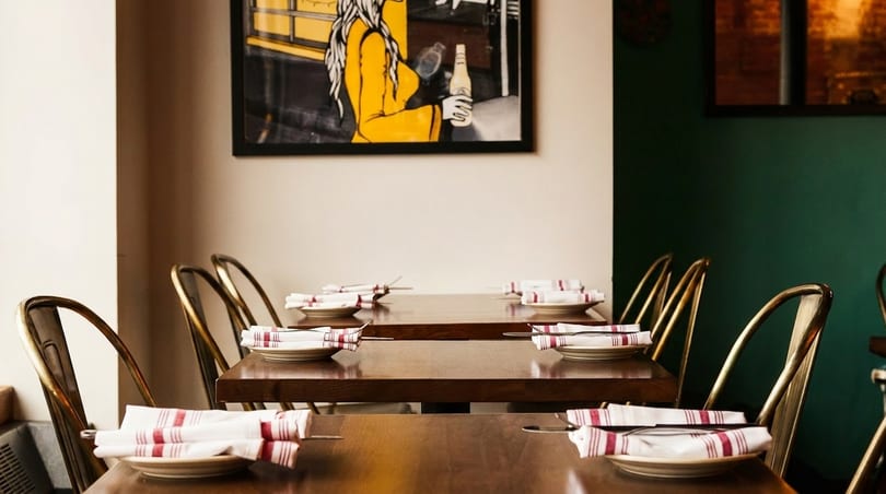Set tables with white and red striped napkins, gold chairs, and a painting of a woman.