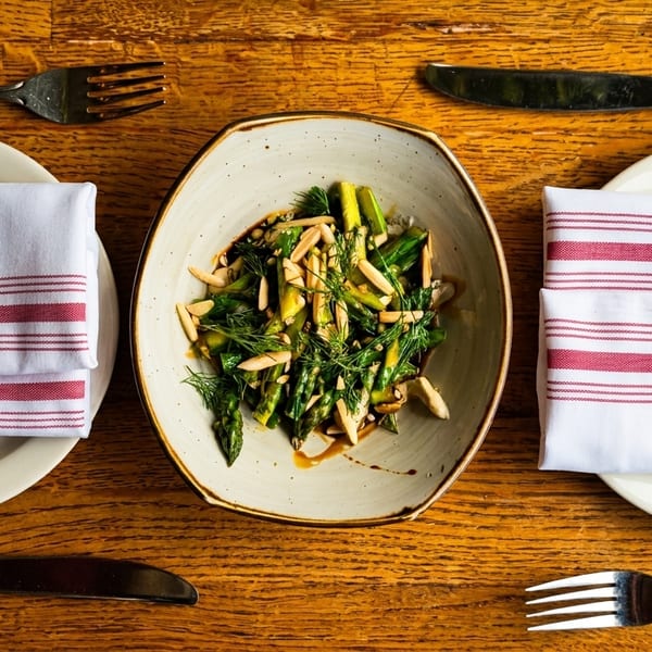 Overhead view of a bowl of asparagus with almonds and dill, flanked by two place settings.