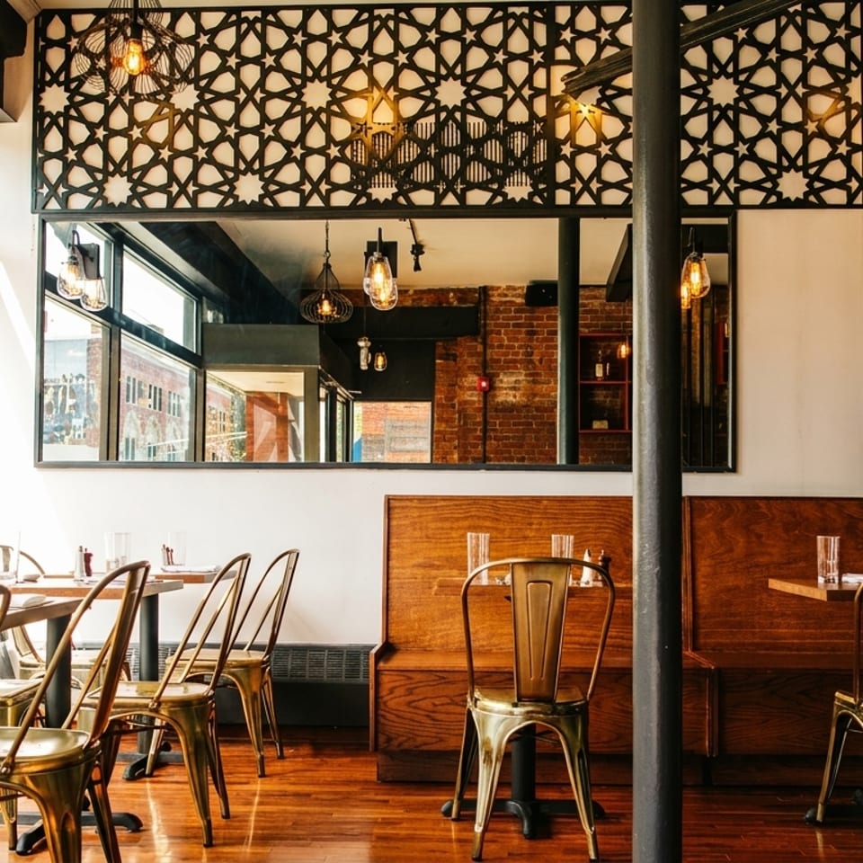 Restaurant interior with tables, gold chairs, large windows, and decorative geometric screens.